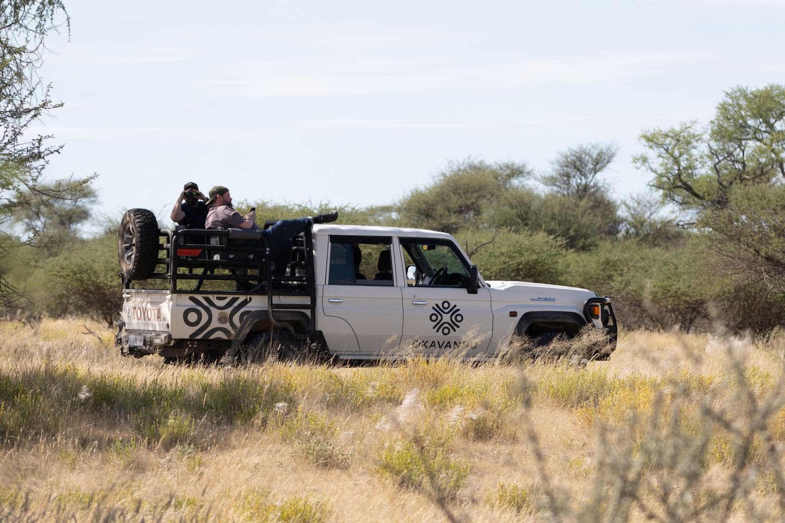Guests on the back of the white Okavandu off-road vehicle look out across the farm's bushland.