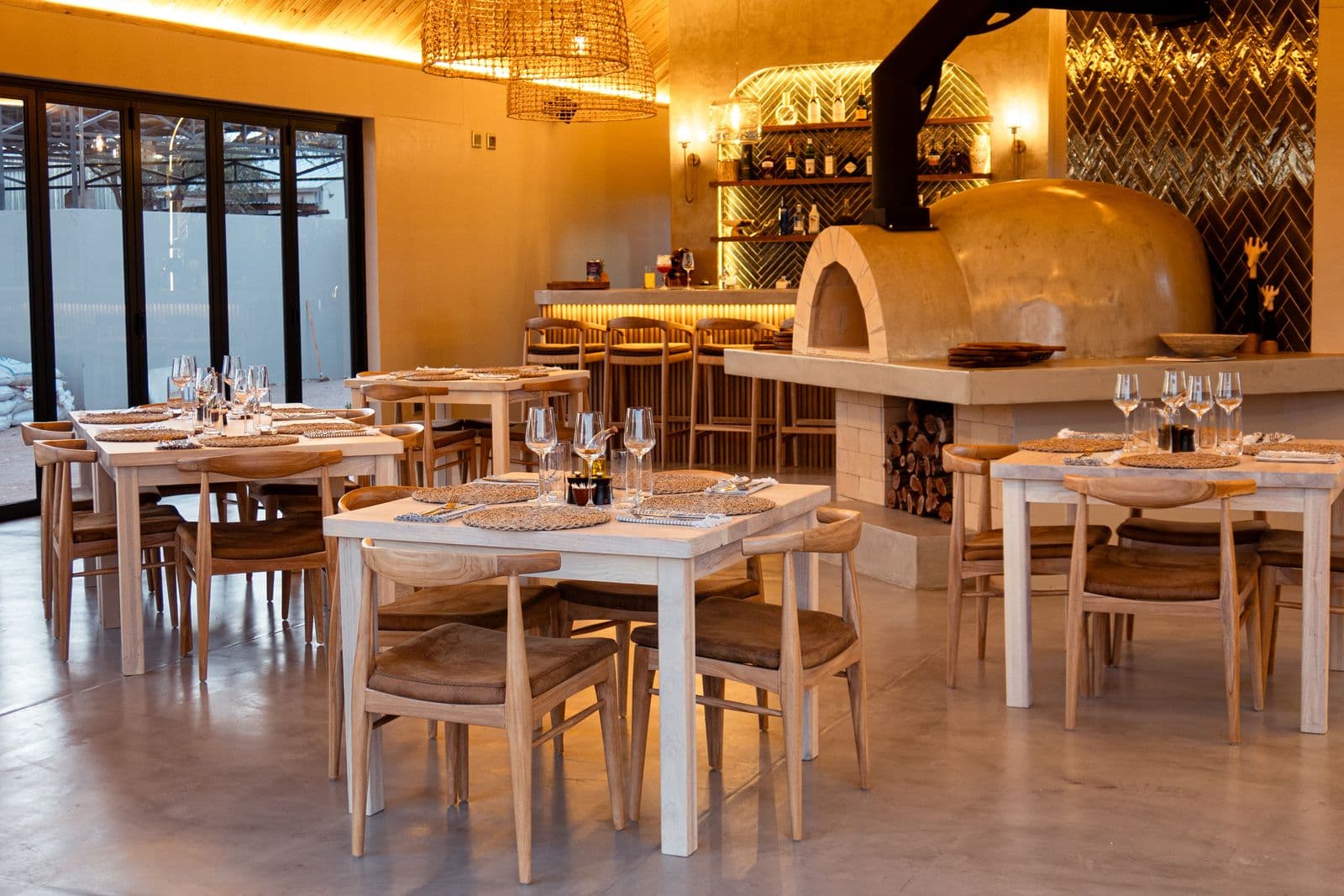 The restaurant in the Lapa in the evening: set tables, with the pizza oven and the lit-up bar behind them.